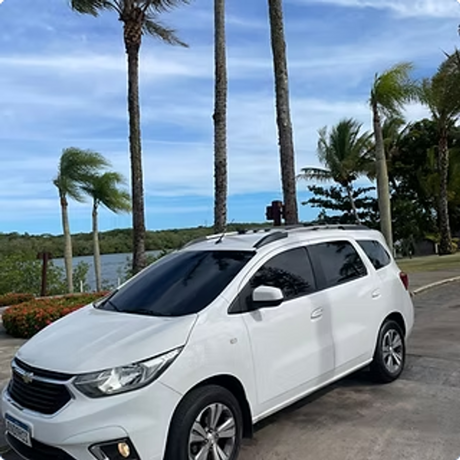 Chevrolet Spin branca estacionada em frente a uma lagoa com coqueiros